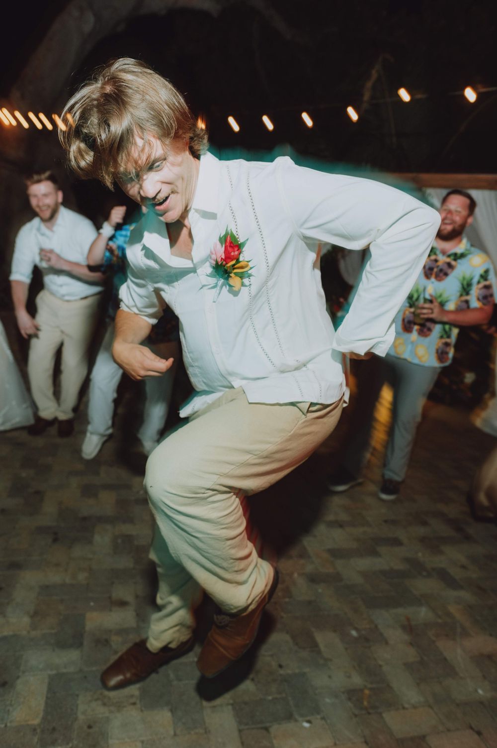 Groomsmen perform coordinated dance moves on a stone patio during wedding reception.