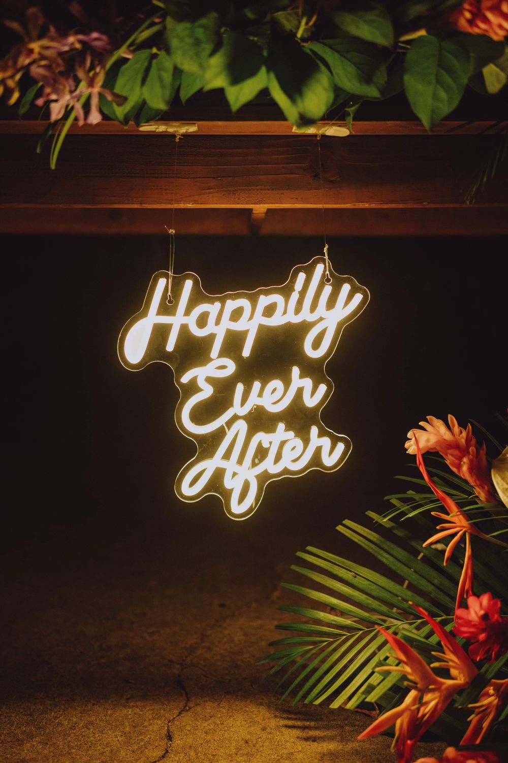 Neon 'Happily Ever After' sign with tropical leaves and flowers as decoration.