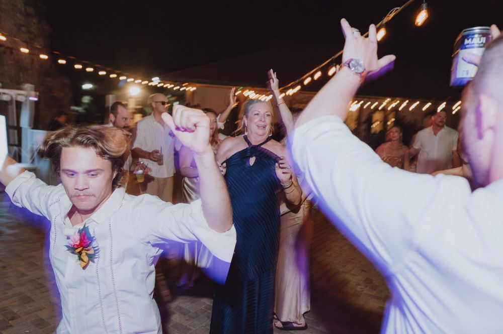 Wedding guests dance energetically on an outdoor patio under string lights.