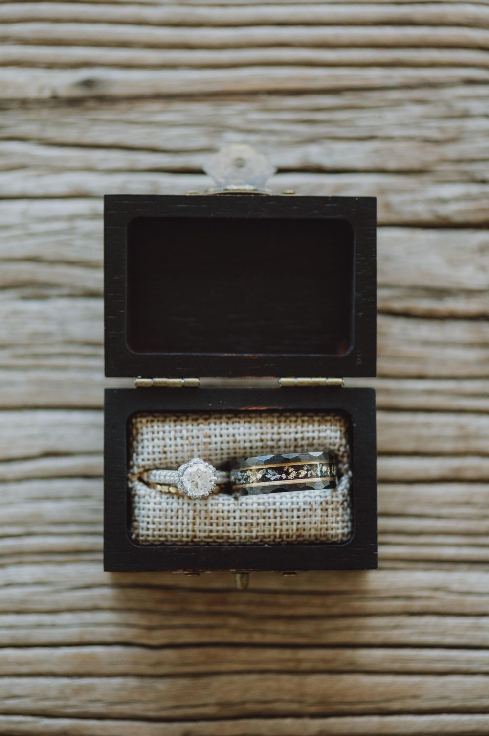 Wedding rings displayed in a rustic wooden box with burlap lining.