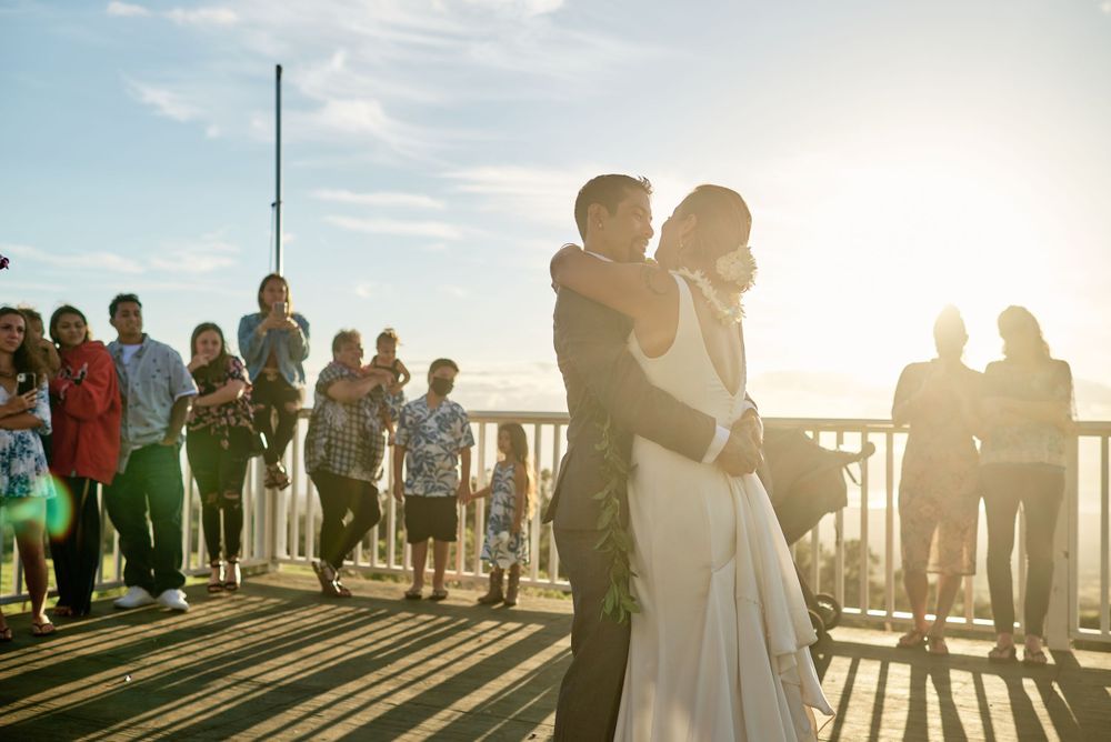 Silhouettes of wedding guests gathered on a deck during golden hour sunset.