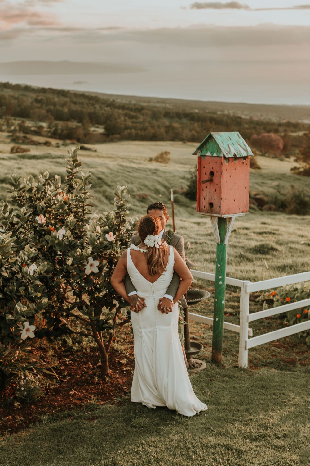 White dress flowing in the golden sunset light on a grassy hilltop with rustic mailboxes and fencing.