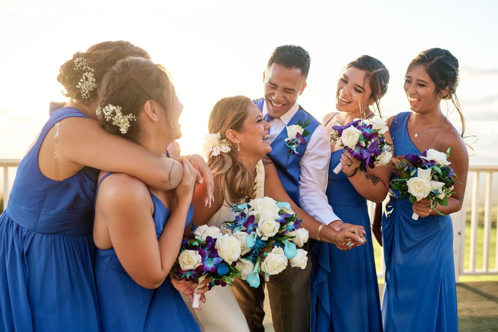 Wedding party members in blue dresses and suits embrace in a group photo.