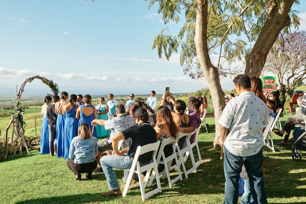 Guests seated in white chairs at an outdoor wedding ceremony with ocean views and palm trees.