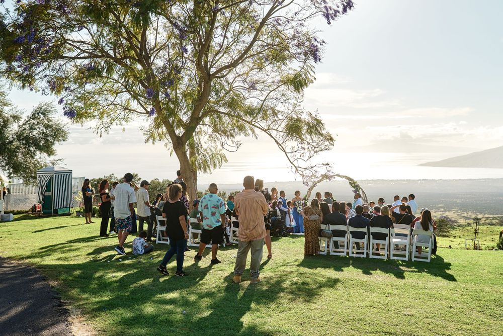 Wedding guests gather for an outdoor ceremony on a scenic hilltop overlooking mountains and ocean views.