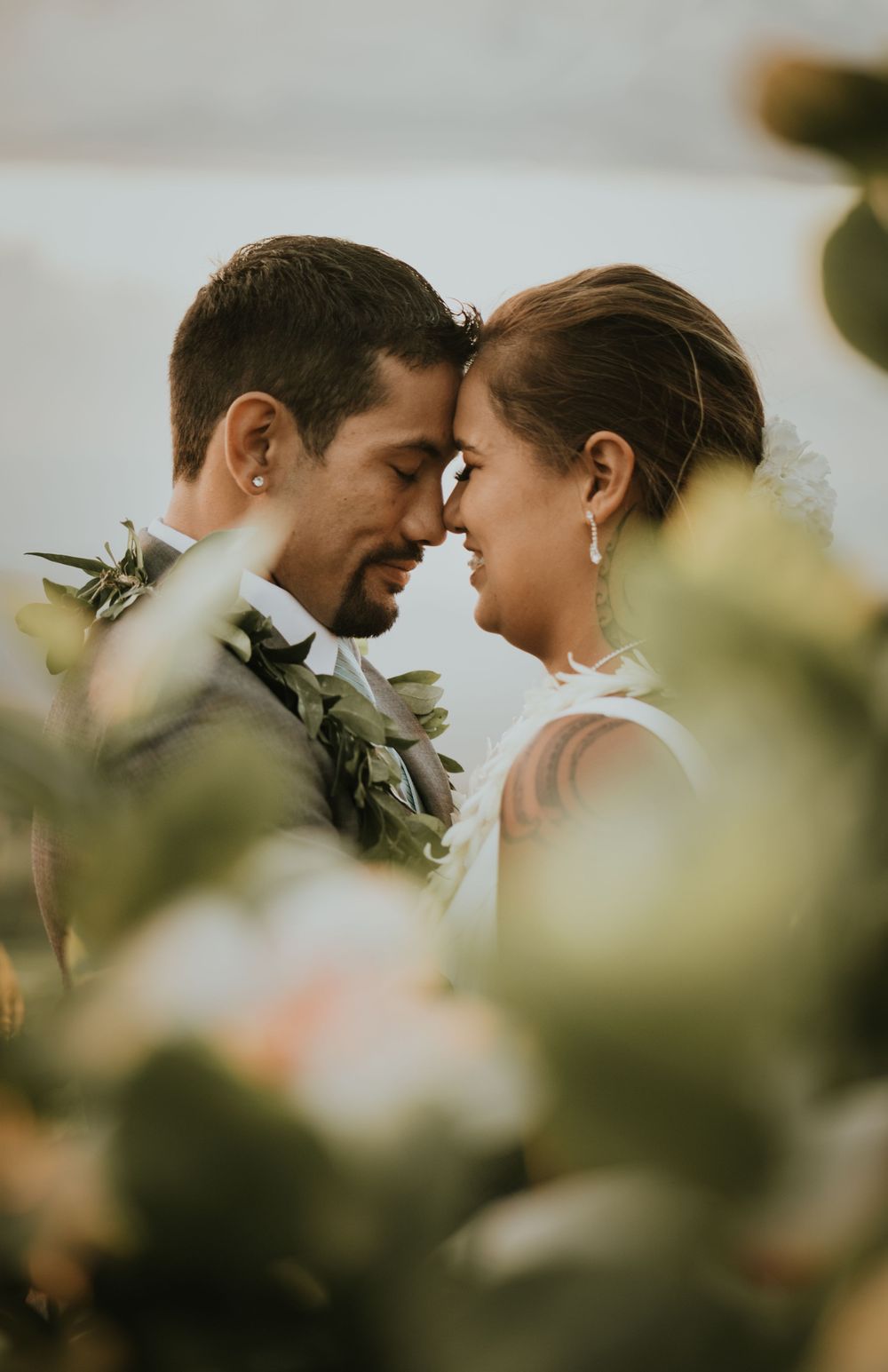 Intimate close-up portrait of a couple wearing green leaf leis against blurred foliage.