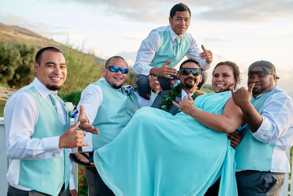 Wedding party members hold up turquoise fabric while posing together outdoors.
