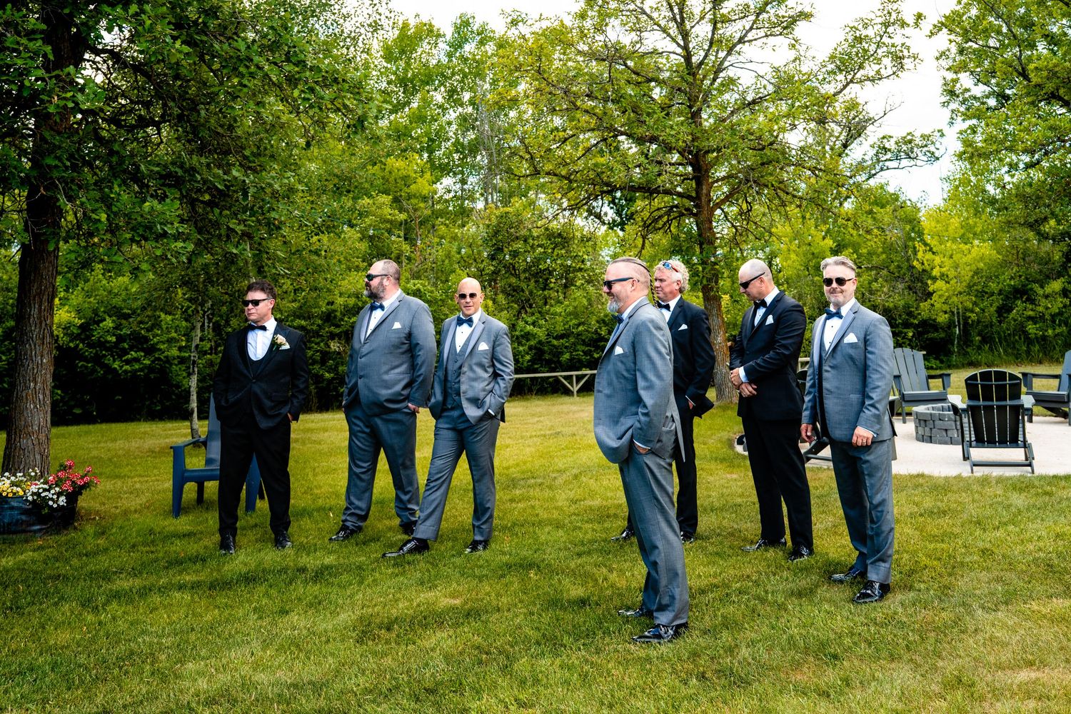 A group of groomsmen in navy blue suits stand on a lush green lawn during an outdoor wedding ceremony.
