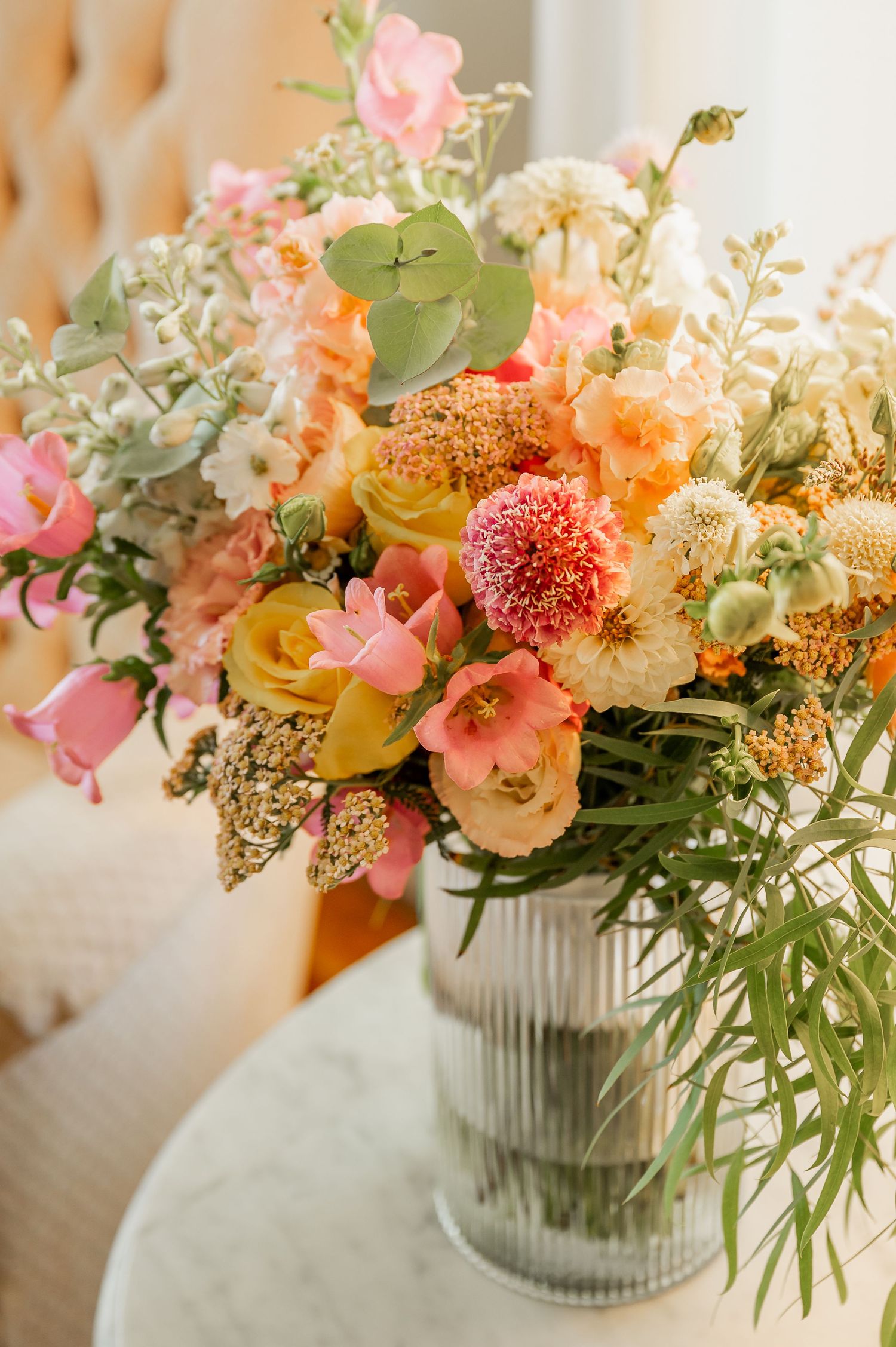 Lush floral centerpiece with coral, pink and yellow blooms in a ribbed glass vase.