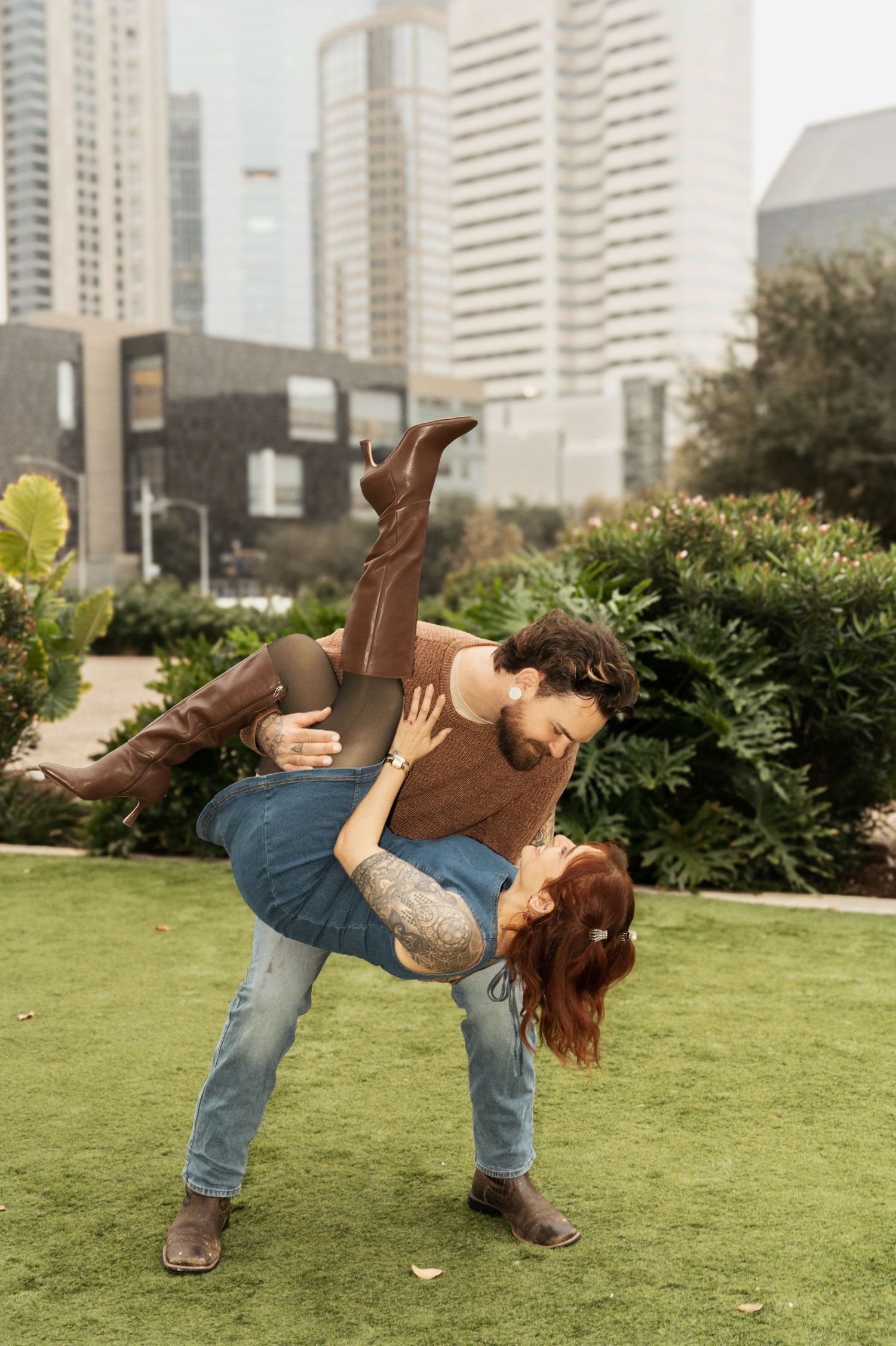 A playful dance dip pose sequence in a city park with skyscrapers and greenery in the background.