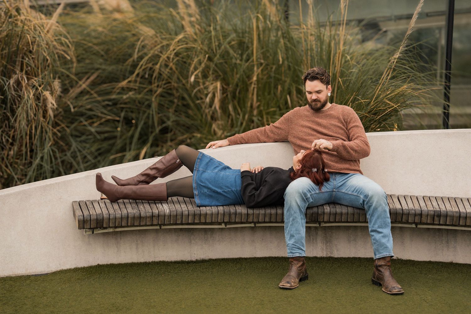 People relaxing on outdoor benches against a backdrop of tall grass and natural scenery.