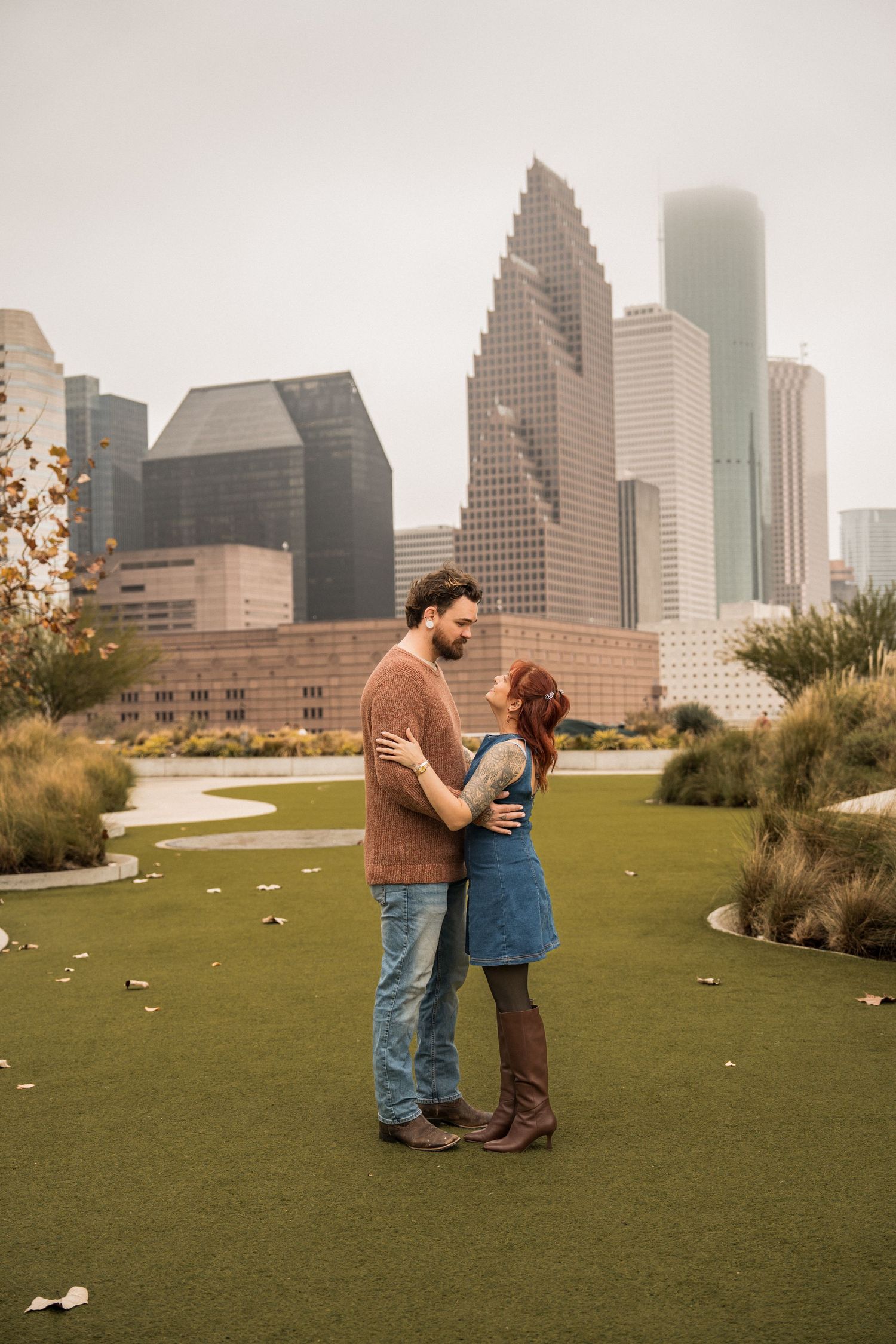 Couple sharing intimate moments on a green lawn with Houston's downtown skyline in the background.