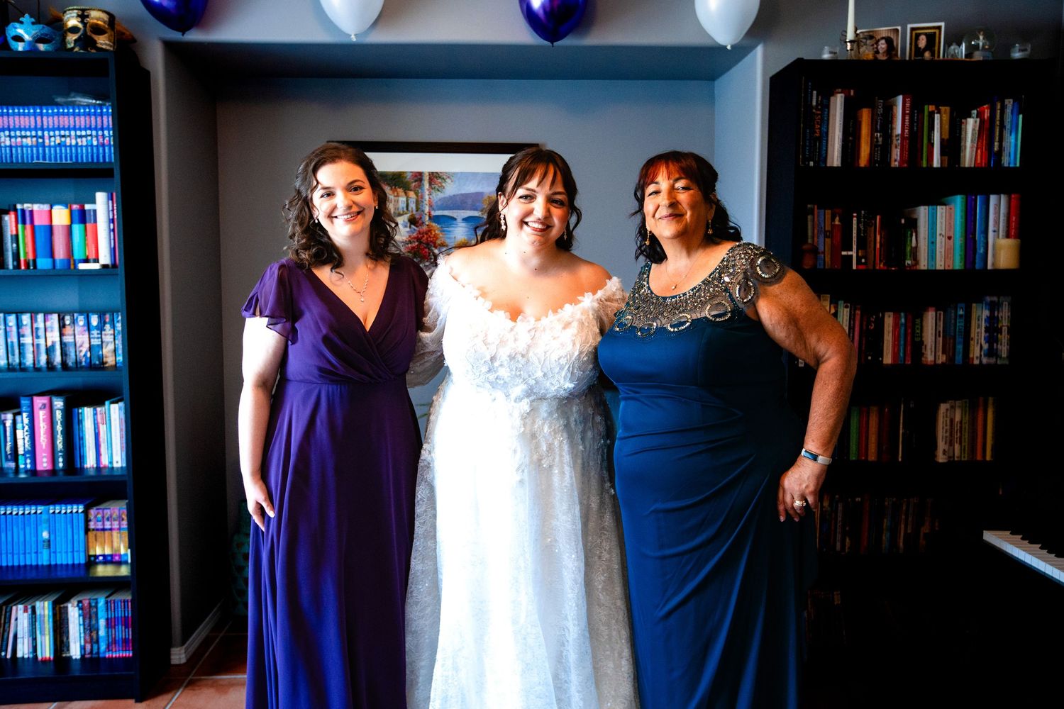 Wedding party poses in front of library bookshelves with bridesmaids wearing navy dresses and bride in white gown.
