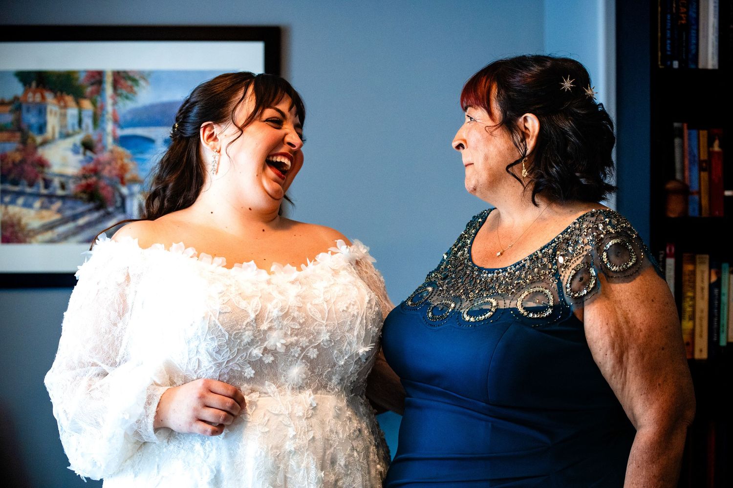 A bride in a white lace gown shares a joyful laugh with someone during a special moment at a wedding celebration.