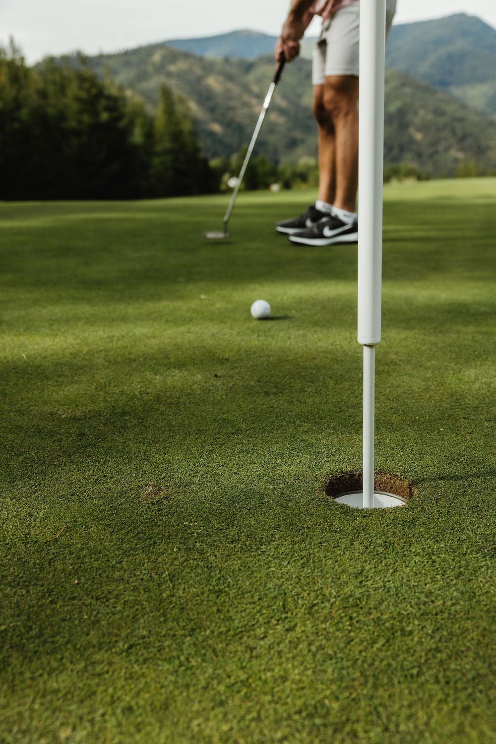 Close-up of a golf ball near the hole on a well-maintained putting green with mountains visible.