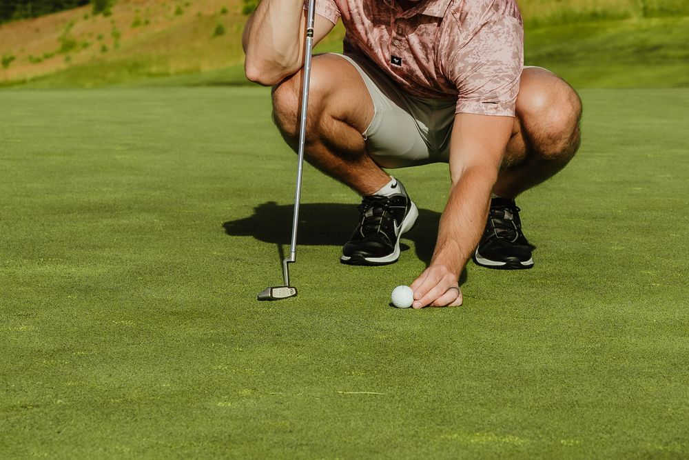 A golfer crouches on a green putting surface to read the break of a putt during a round of golf.