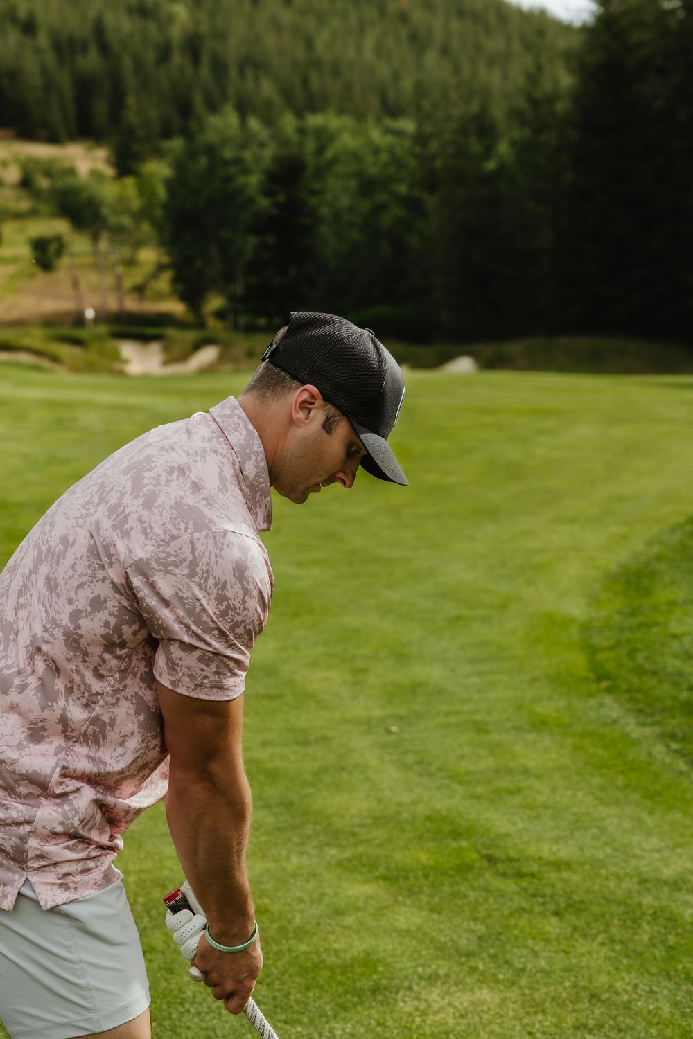 Golfer in a patterned shirt prepares to take a shot on a scenic mountain course.