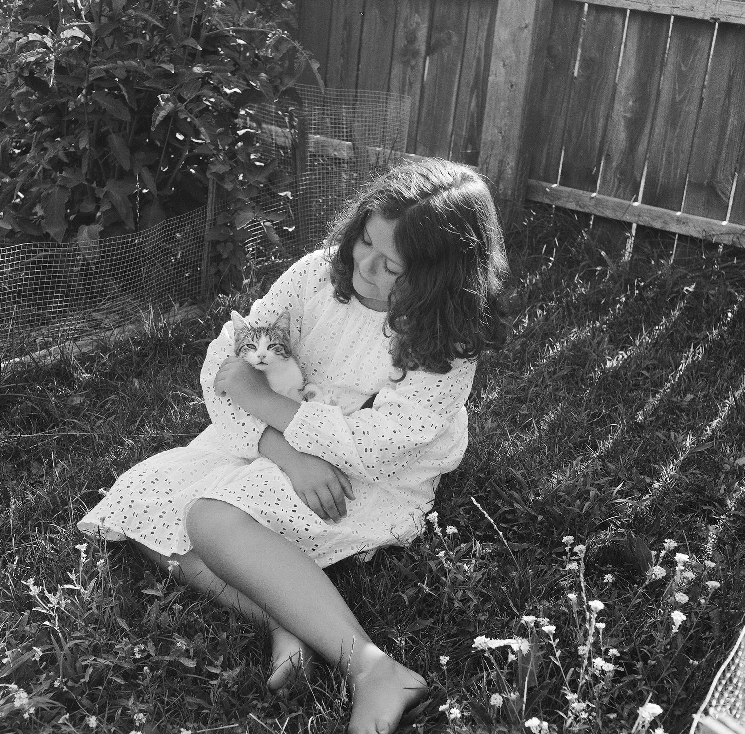 A sequence of black and white photos showing someone in a white eyelet dress lying in a garden setting.