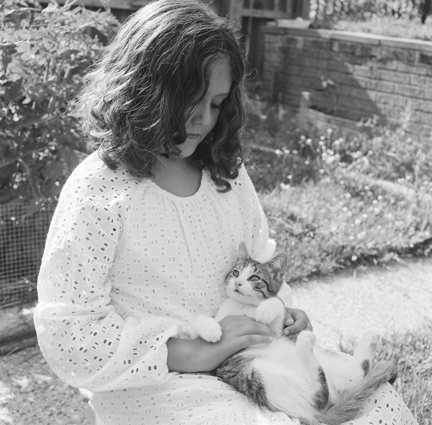 A sequence of black and white photos showing someone in a white eyelet dress sitting outdoors on grass.
