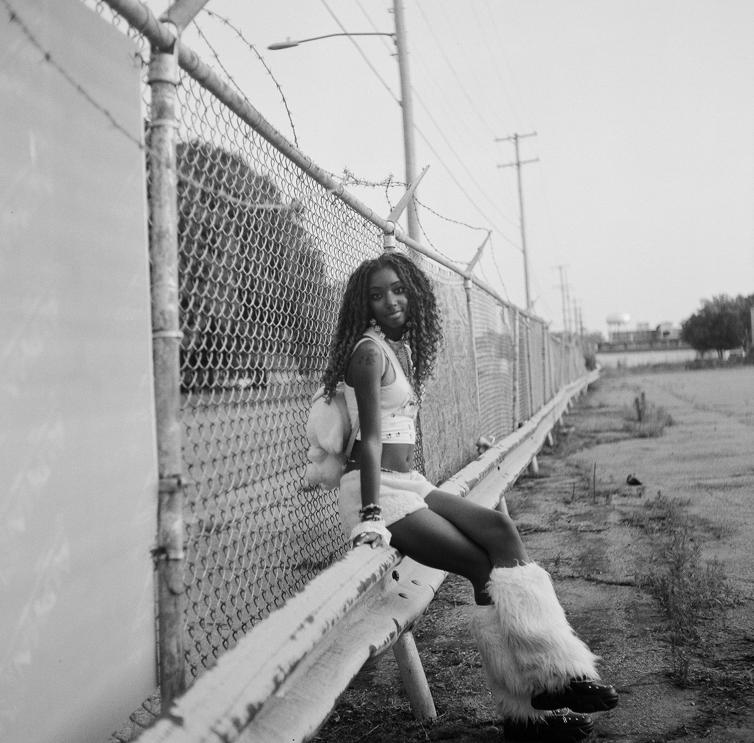 Black and white photos of someone posing along a chain link fence in an urban setting.