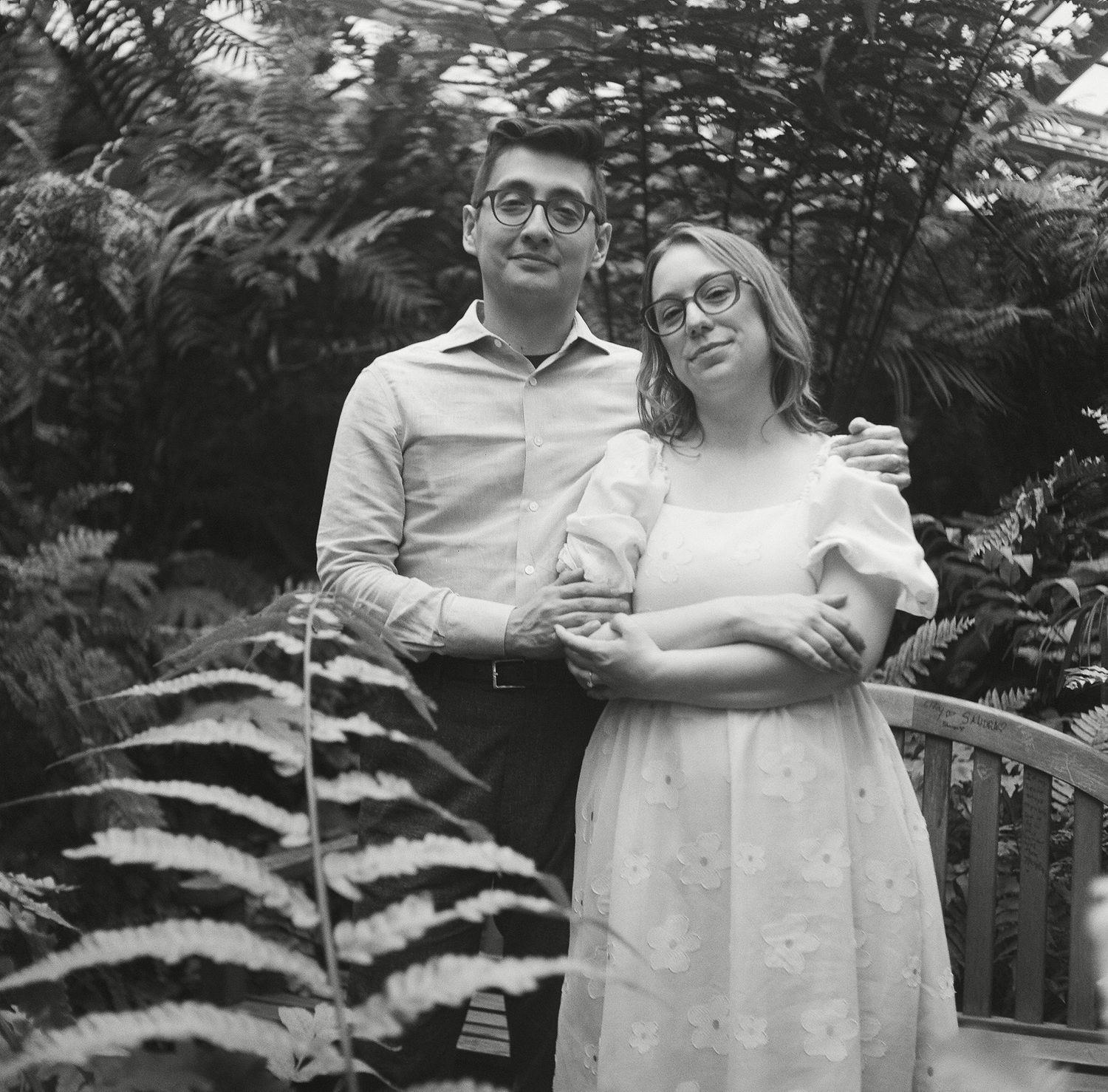Black and white photo series showing a couple embracing in a garden setting with lush foliage in the background.