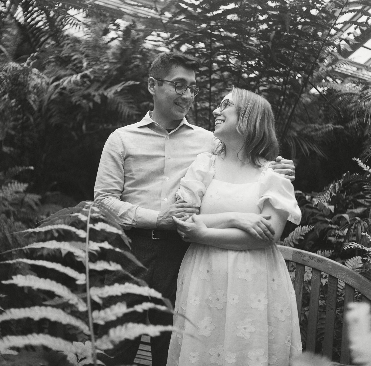 Black and white photo series showing a couple embracing in a garden setting with lush greenery surrounding them.