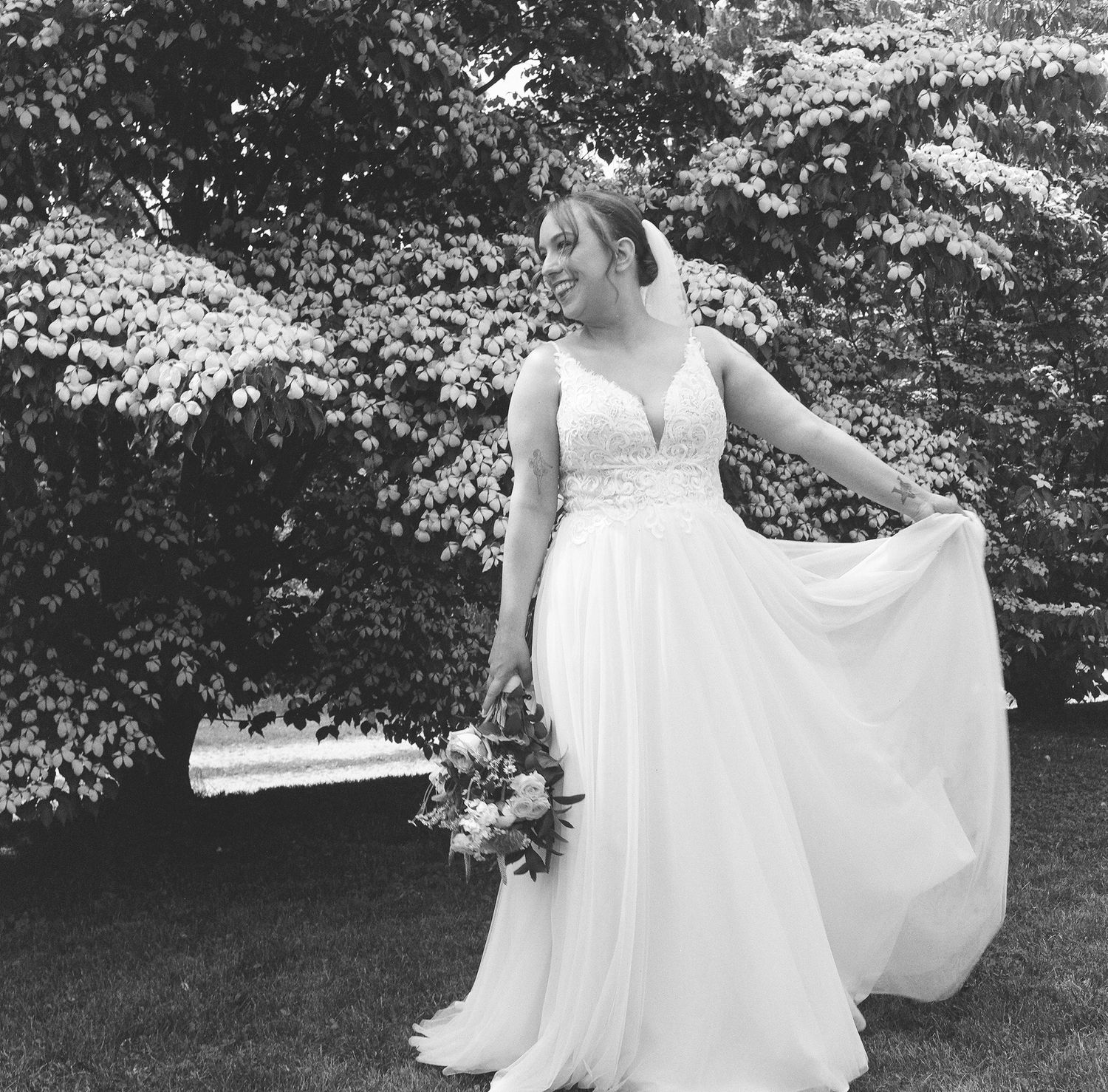 A bride in a flowing white gown twirls gracefully in a garden setting with blooming trees in the background.
