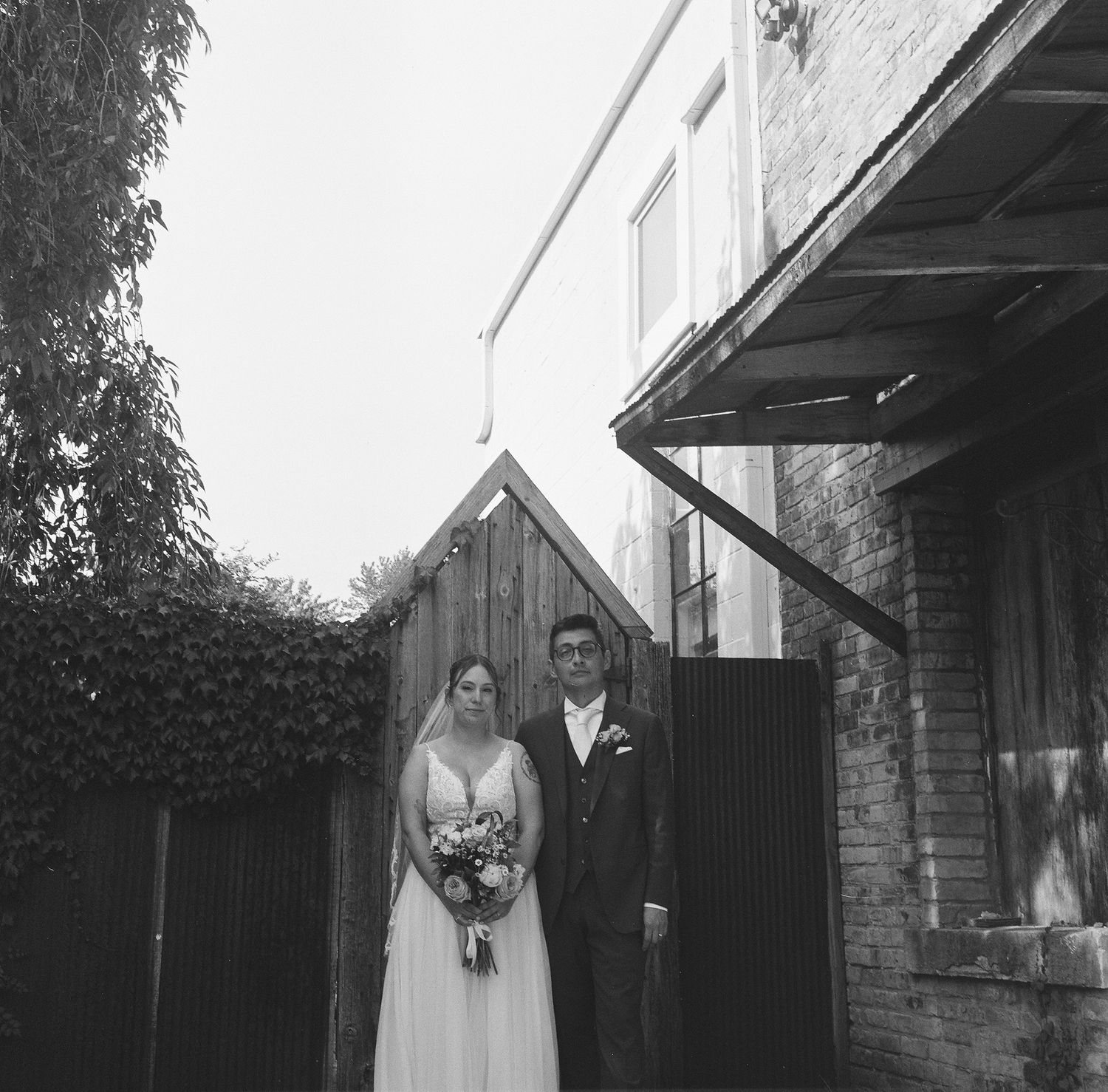 Black and white wedding photos showing a couple in formal attire walking and posing outside a rustic building.