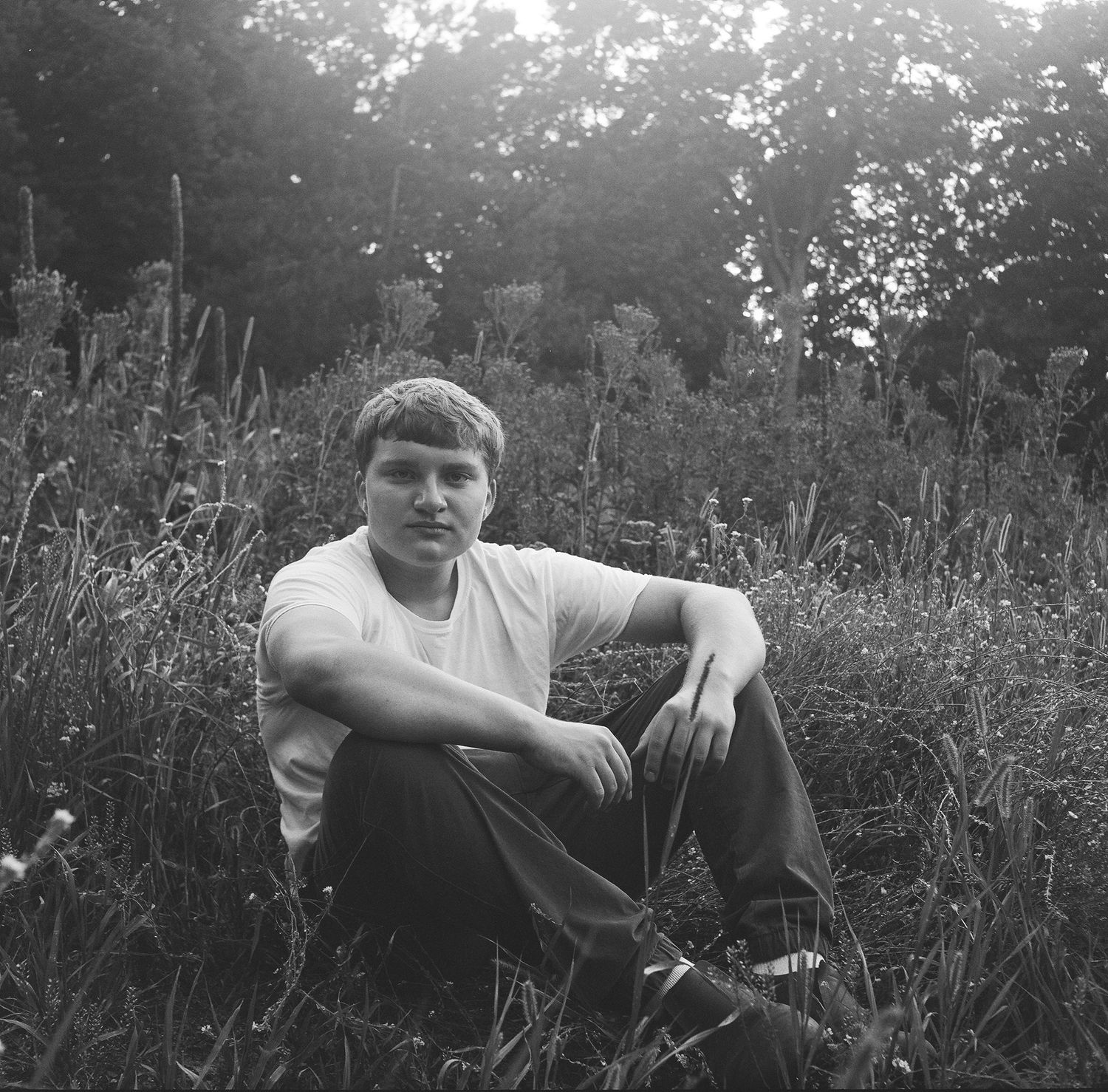 A black and white photo series shows someone picking berries in tall grass and wildflowers on a sunny day.