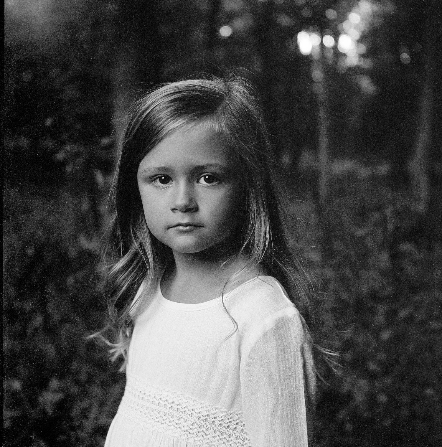 Black and white artistic portrait series showing a child in a white dress against a dark background.