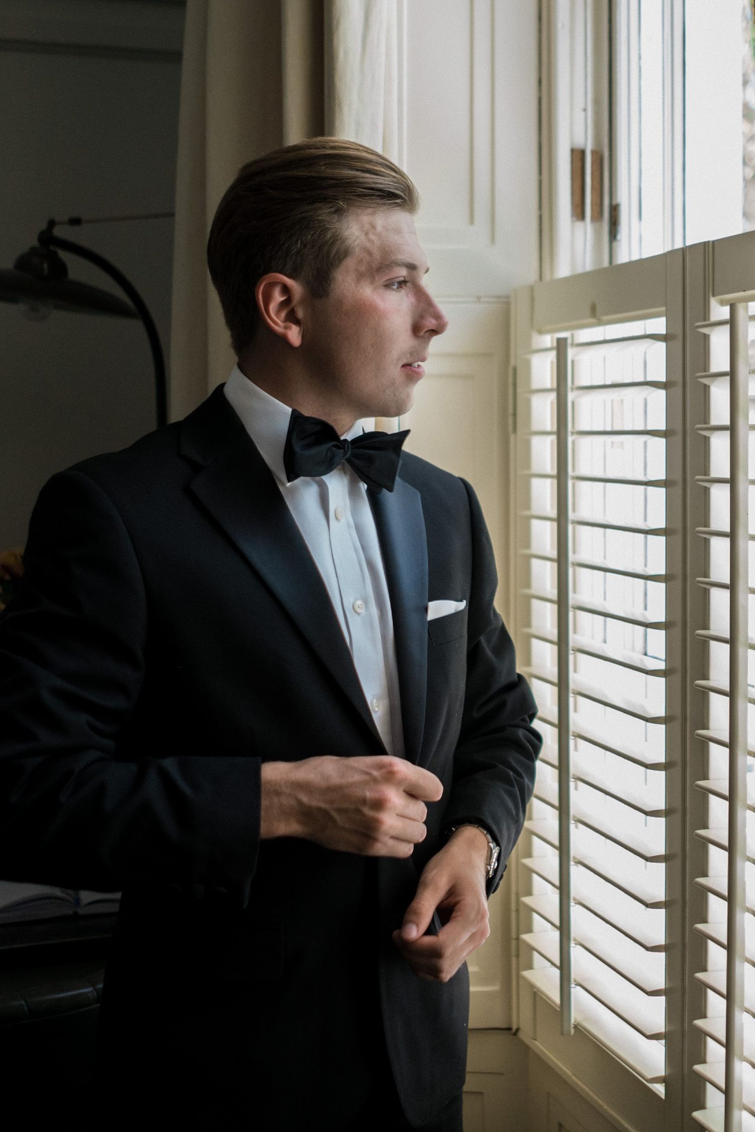 A person in a black tuxedo and bow tie stands by a window with venetian blinds, shown in multiple angles.