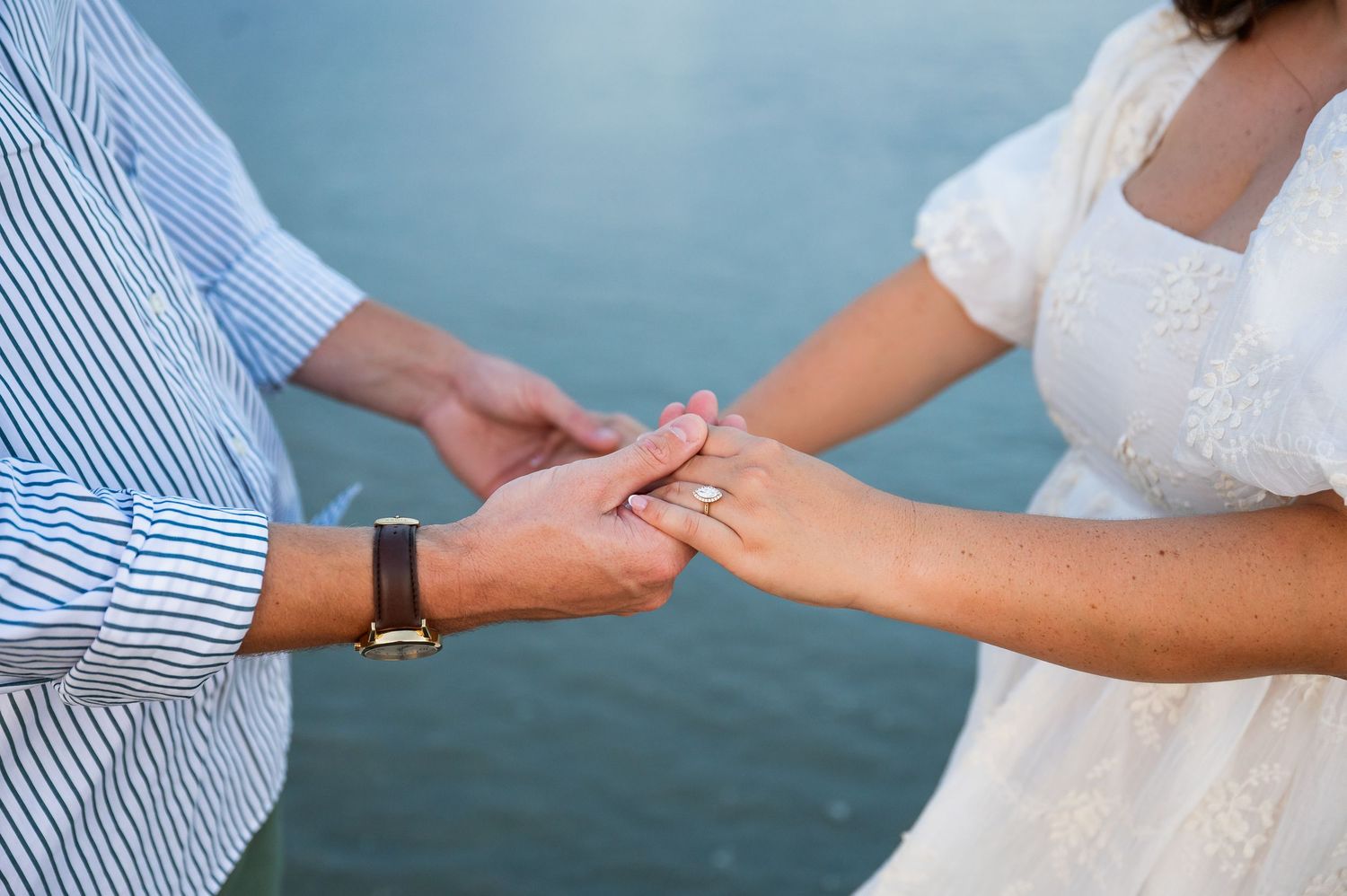 Close-up of hands holding each other against blue ocean background.
