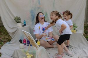 Group of friends having fun with colorful paint during an outdoor paint party celebration on white sheets.