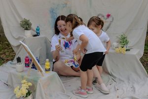 Children participate in a hands-on arts and crafts activity at white tables outdoors with colorful art supplies.