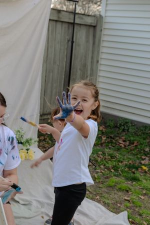 A sequence showing a child in a white shirt with colorful paint on their hands making expressive gestures outdoors.