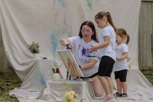 A group of students works on an art project with paint on a white backdrop during a creative workshop session.