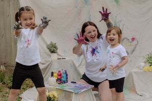 Children in white t-shirts and black shorts play with colorful paint during an outdoor art activity.