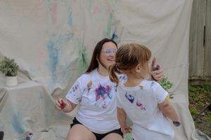 Two children wearing white shirts play with colorful powder during a festive outdoor celebration.