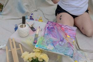 Close-up view of hands working with colorful art materials and wooden craft sticks on a light surface.