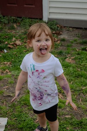 A joyful moment captured outdoors showing playful energy and a paint-stained white t-shirt against a green lawn background.