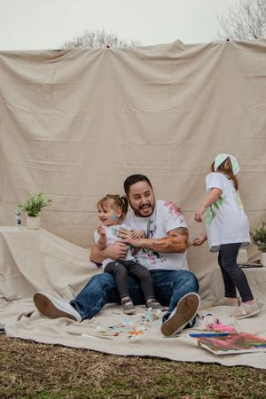 A playful family photo sequence shows parents and child tumbling and playing together on a beige blanket outdoors.
