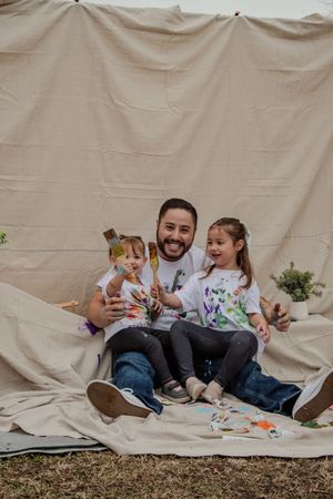 Family enjoying a playful moment together while sitting on a blanket outdoors against a beige backdrop.