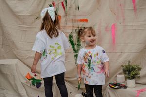 Children wearing white t-shirts paint together during a creative art activity with colorful paints and brushes.
