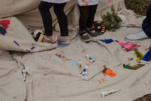 People's feet are visible on a paint-splattered tarp during a creative art activity.