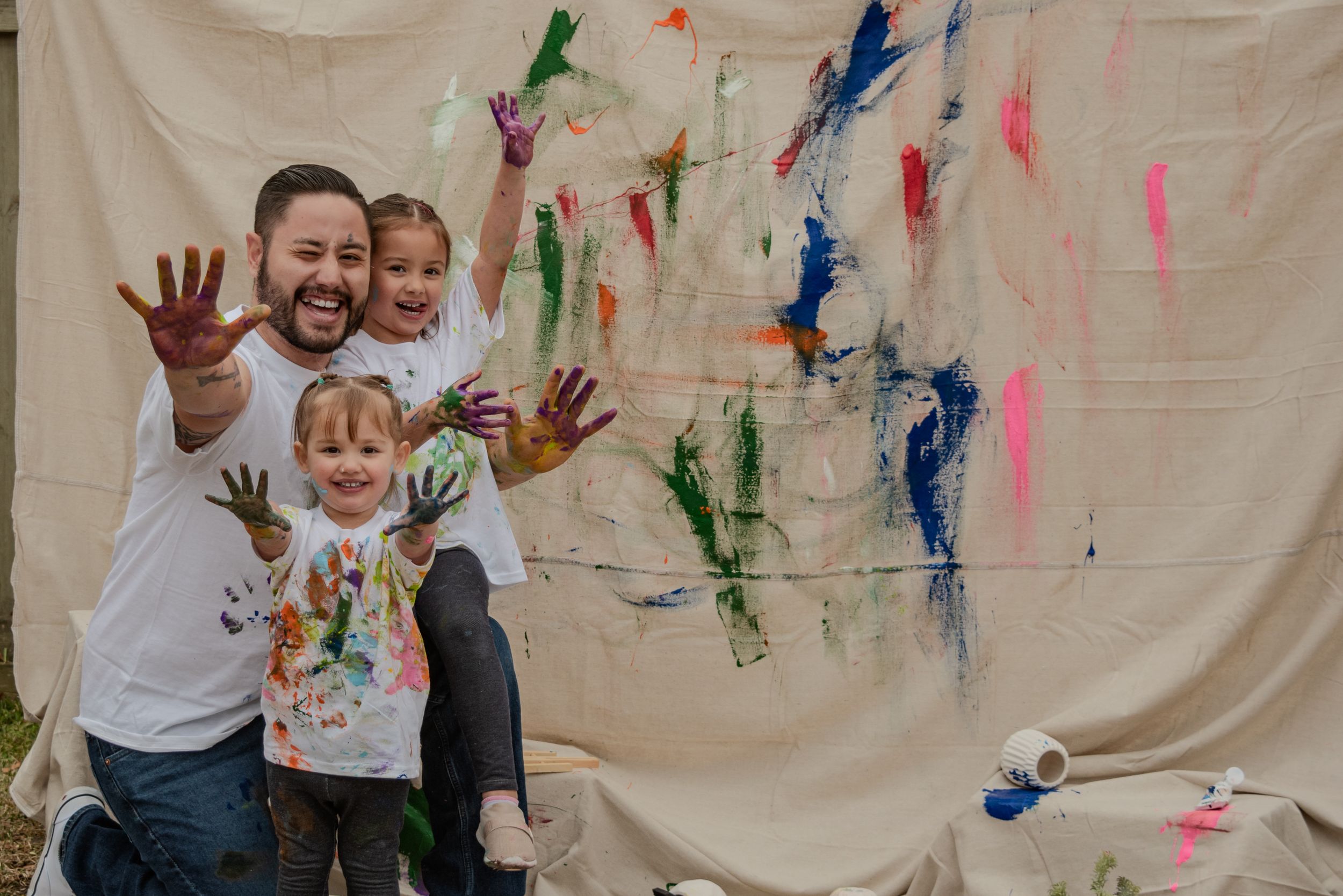 People in white shirts create colorful handprint art on a light colored backdrop during a fun painting activity.