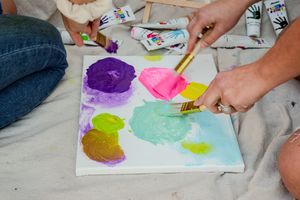 Hands work on colorful watercolor paintings laid out in a row on a white surface.
