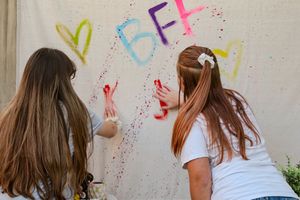 Four images showing someone in a white shirt making colorful paint splatter art on a beige wall.