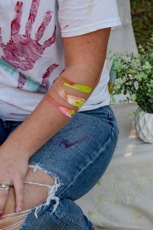 Close-up shots showing hands covered in vibrant paint colors while creating artwork on a white surface.