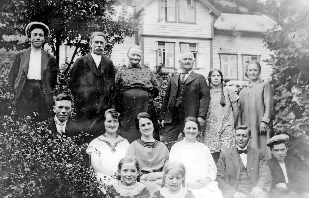 A vintage black and white group photograph showing people posed together in front of a house.