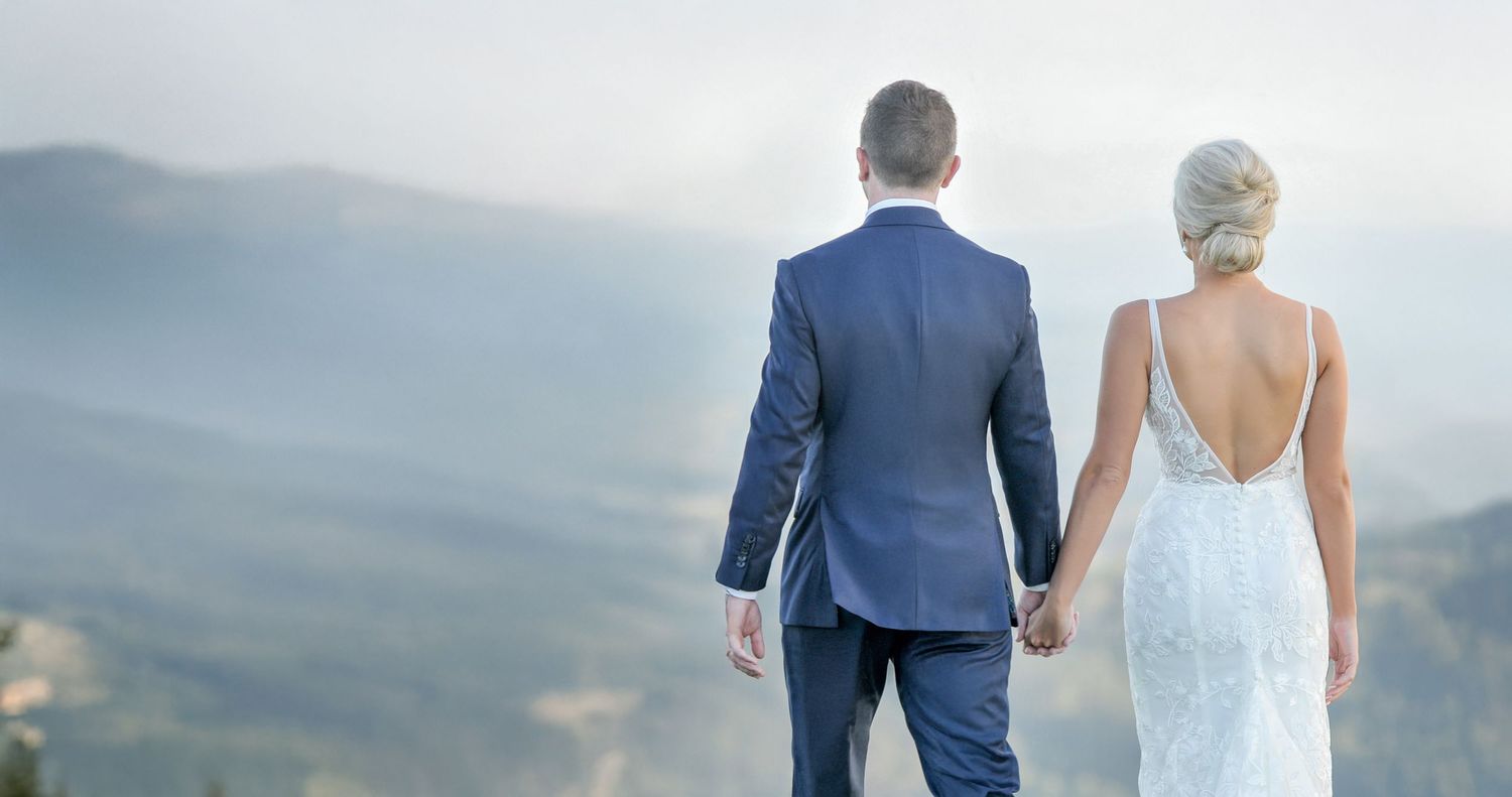 Bride and groom holding hands overlooking stunning misty mountain valley in wedding attire.